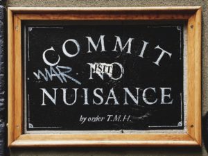 Image, blackboard sign saying "Commit no nuisance" with graffiti on it.