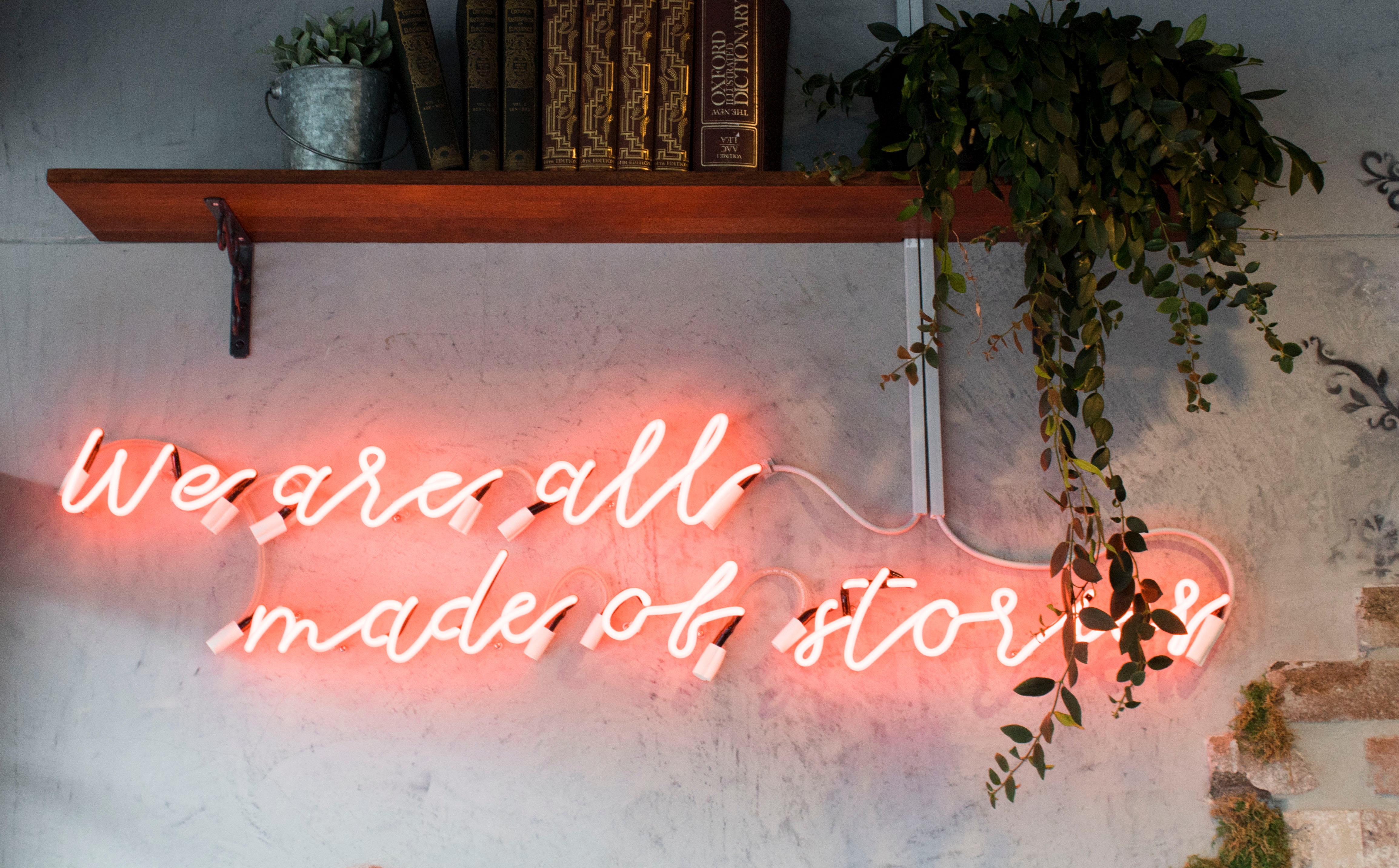 Pink neon sign on wall saying 'We are all made of stories'