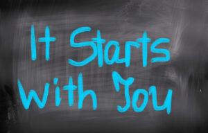 Blue script on blackboard says 'It starts with you'