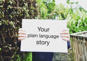 Hands holding a sign saying 'Your plain language story'